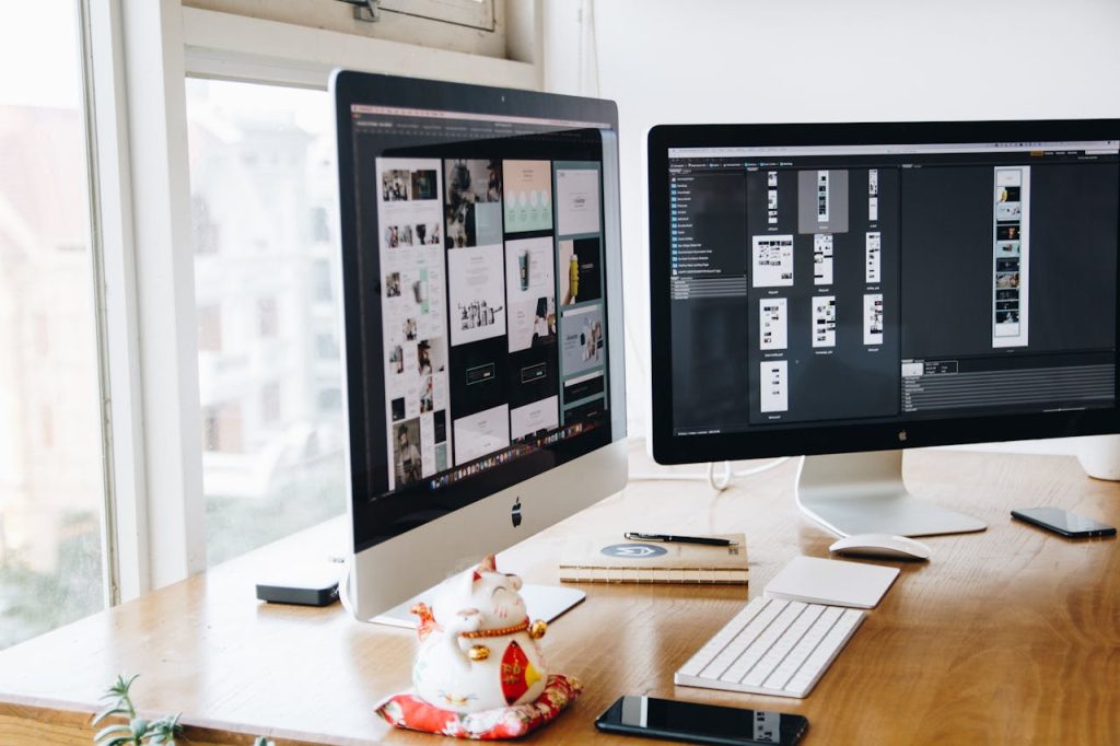 silver-imac-on-top-of-brown-wooden-table-326502 A sleek modern office setup featuring dual monitors, Apple devices, and creative decor in an indoor workspace.